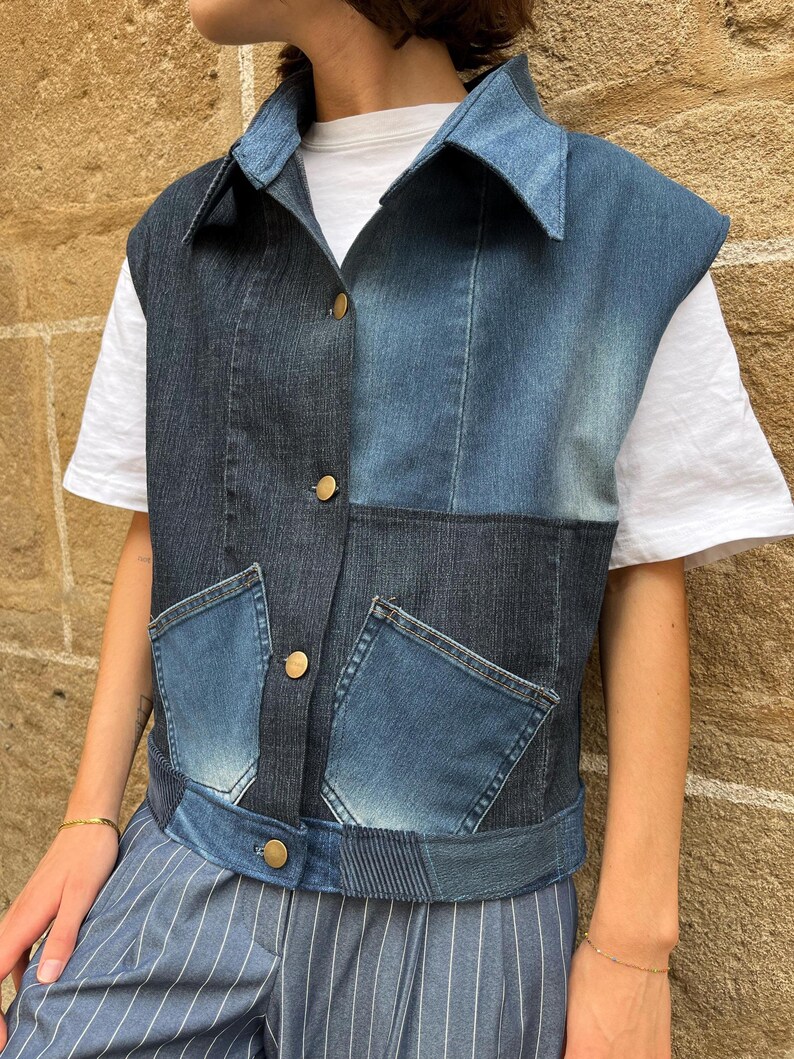 May include: A denim vest with a patchwork design in various shades of blue. The vest features a collar, two front pockets, and gold-colored buttons. The garment is worn over a white t-shirt and blue striped pants.