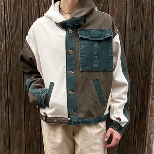 May include: A color-blocked jacket with a white, brown, and denim blue design. The jacket features a hood, button closures, and a pocket on the chest. The sleeves have denim blue accents. The jacket is a stylish outerwear piece.