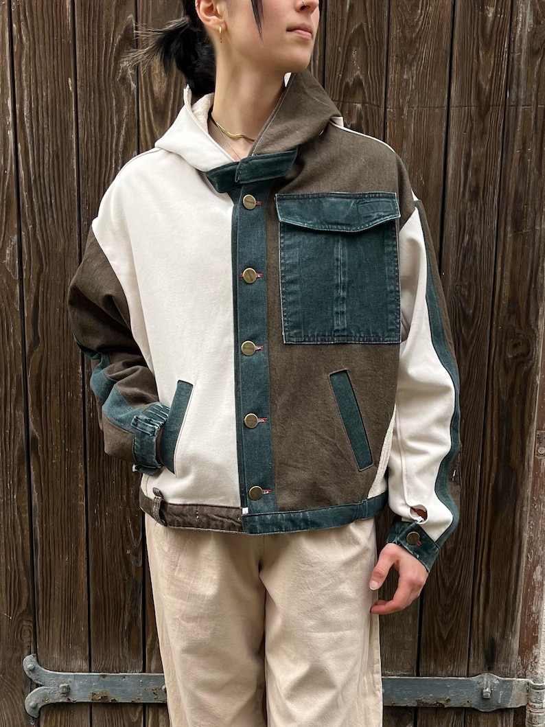 May include: A color-blocked jacket with a white, brown, and denim blue design. The jacket features a hood, button closures, and a pocket on the chest. The sleeves have denim blue accents. The jacket is a stylish outerwear piece.