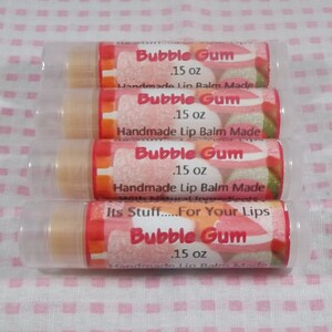 Puede incluir: Cuatro tubos transparentes de bálsamo labial con un diseño de chicle rosa y blanco. Cada tubo está etiquetado con "Bubble Gum" y dice "Bálsamo labial hecho a mano con ingredientes naturales". El tubo inferior también dice "Its Stuff.....For Your Lips".