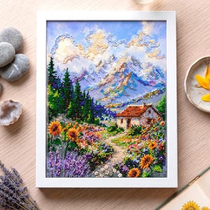 May include: A framed diamond painting depicting a mountain landscape with a small house, a field of sunflowers, and lavender. The artwork features a blue sky with clouds, green pine trees, and a dirt path leading to the house in a white frame.