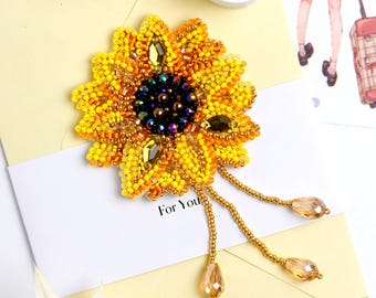 May include: A beaded sunflower brooch with yellow, orange, and dark green beads. The brooch has dangling gold-colored strands with teardrop-shaped beads. The words "For You" are visible on the card.