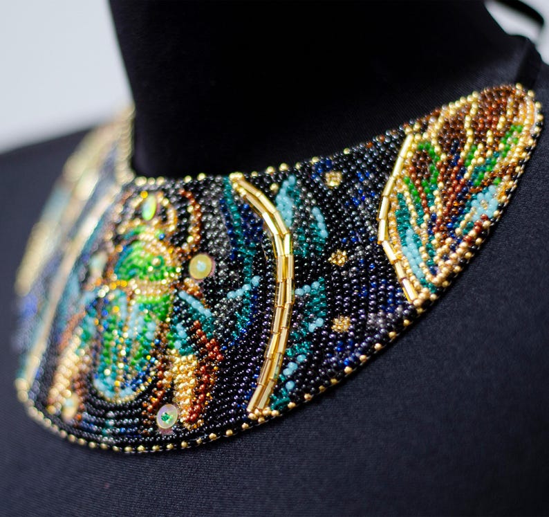 K&ouml;nnte beinhalten: Eine schwarze, blaue, gr&uuml;ne und goldene Perlenkette mit einem gro&szlig;en, detaillierten Design eines Skarab&auml;us.
