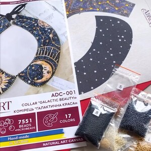 May include: A beading kit for a collar with a celestial theme. The kit includes a canvas, beads in various colors, and instructions. The collar design features a crescent moon, stars, and a sun. The kit is labeled "ADC-001 Collar "Galactic Beauty" Komirets "Galaktichna Krassa" 7551 Beads Microbeads 17 Colors Natural Art Canvas"