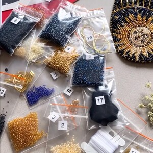 May include: A close-up of a beading kit with various colors of beads in small plastic bags. The bags are labeled with numbers. There is also a spool of white thread and a needle.