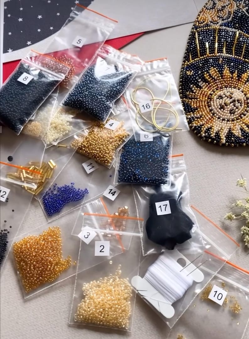 May include: A close-up of a beading kit with various colors of beads in small plastic bags. The bags are labeled with numbers. There is also a spool of white thread and a needle.