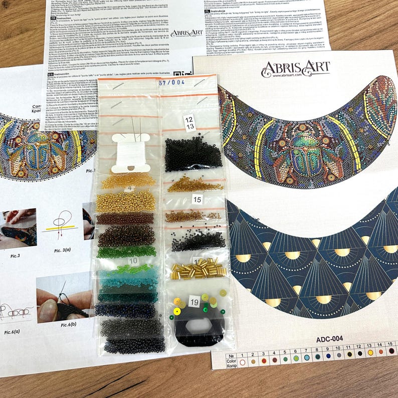 K&ouml;nnte beinhalten: Ein Perlen-Set f&uuml;r eine Halskette mit einem farbenfrohen K&auml;fer-Design. Das Set enth&auml;lt ein Muster, Perlen in verschiedenen Farben und Nadeln. Das Muster zeigt einen farbenfrohen K&auml;fer mit einem blauen, gr&uuml;nen und gelben Design. Die Perlen befinden sich in kleinen Plastikt&uuml;ten, die mit Nummern beschriftet sind. Das Set ist mit "ADC-004" gekennzeichnet.