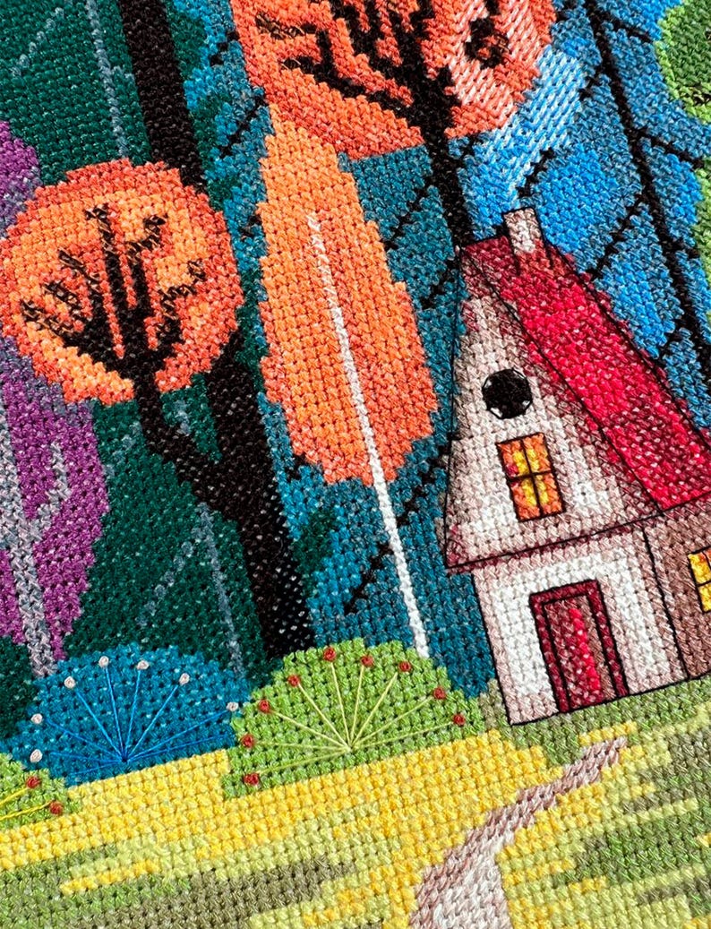 May include: A cross-stitch embroidery depicting a colorful forest scene with a small house in the foreground. The house has a red roof, white walls, and a black door. The forest is filled with trees in shades of green, blue, orange, and purple. The ground is a bright yellow with a path leading to the house.