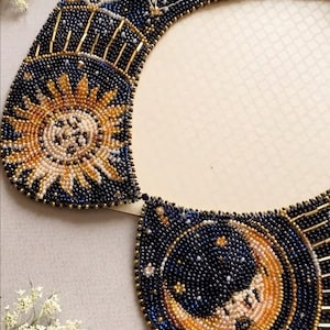 May include: A beaded collar with a celestial design featuring a sun and moon with stars on a dark blue background.