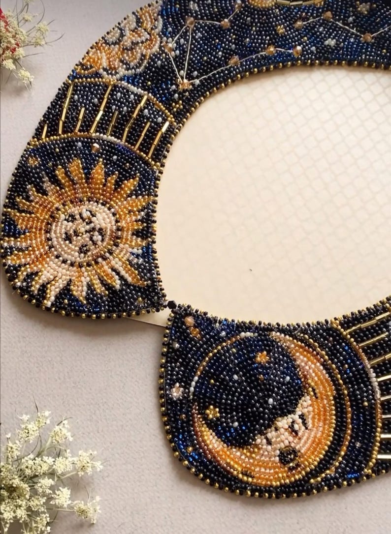 May include: A beaded collar with a celestial design featuring a sun and moon with stars on a dark blue background.
