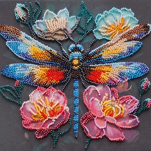 Peut inclure: Une libellule en perles avec des ailes bleues, jaunes, rouges et brunes entourées de fleurs en perles roses, bleues et blanches.