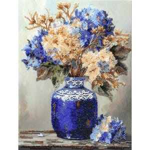 May include: A beaded artwork depicting a bouquet of flowers in a blue vase. The flowers are a mix of blue, beige, and gold beads. The vase is a deep blue with white detailing. A small bouquet of flowers sits next to the vase.
