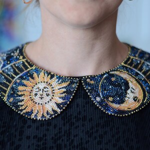 May include: A black collar with a beaded design featuring a sun and moon motif. The beads are in shades of blue, gold, and white.