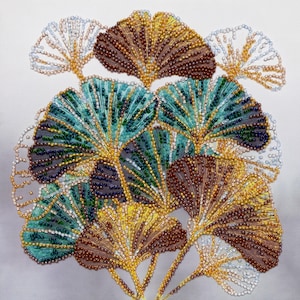 Könnte beinhalten: Eine Nahaufnahme eines Perlenkunstwerks, das einen Cluster von Ginkgoblättern darstellt. Die Blätter bestehen aus kleinen, bunten Perlen in Grün-, Braun- und Goldtönen. Das Kunstwerk ist ein wunderschönes Beispiel für Perlen Stickerei.