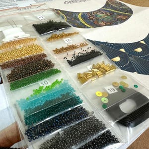 K&ouml;nnte beinhalten: Nahaufnahme eines Sets aus Perlen und Pailletten in verschiedenen Farben und Gr&ouml;&szlig;en, sortiert in durchsichtigen Plastikt&uuml;ten. Die Beutel sind mit Nummern beschriftet und die Perlen sind in Reihen angeordnet. Das Bild zeigt auch ein gedrucktes Muster f&uuml;r eine Perlenkette.
