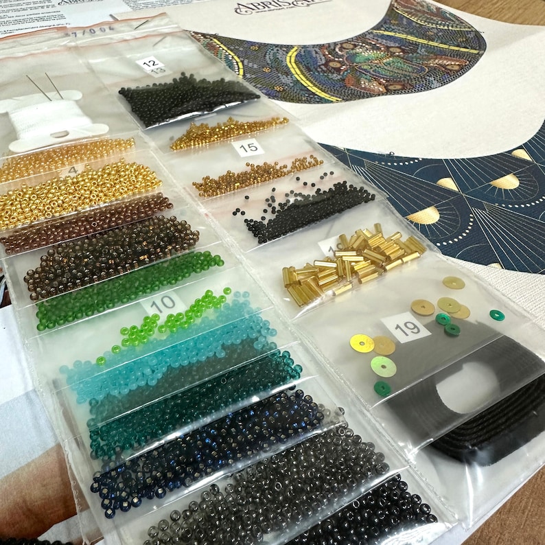 K&ouml;nnte beinhalten: Nahaufnahme eines Sets aus Perlen und Pailletten in verschiedenen Farben und Gr&ouml;&szlig;en, sortiert in durchsichtigen Plastikt&uuml;ten. Die Beutel sind mit Nummern beschriftet und die Perlen sind in Reihen angeordnet. Das Bild zeigt auch ein gedrucktes Muster f&uuml;r eine Perlenkette.