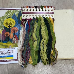 May include: Cross stitch kit with a colorful forest scene, a small house, and a variety of floss colors. The kit includes a piece of Aida cloth, a needle, and instructions. The kit is labeled "Abris Art" and "Hand-made in Ukraine".