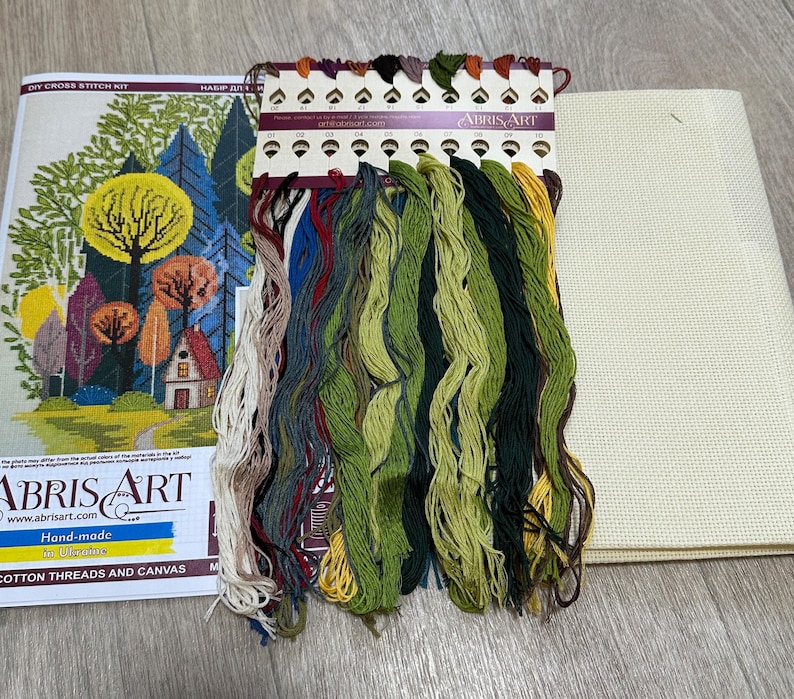 May include: Cross stitch kit with a colorful forest scene, a small house, and a variety of floss colors. The kit includes a piece of Aida cloth, a needle, and instructions. The kit is labeled "Abris Art" and "Hand-made in Ukraine".