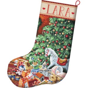 Pode incluir: Uma meia de Natal com um design em ponto cruz de uma árvore de Natal verde decorada, um cavalo de balanço branco e vários brinquedos. A parte superior é creme com bordas vermelhas e o nome LARA impresso em vermelho com pequenos corações.