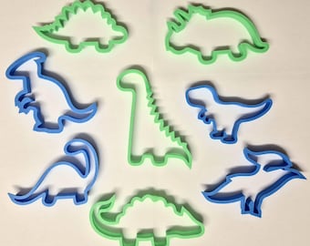 Könnte beinhalten: Satz mit acht Dinosaurier-Ausstechformen, vier blaue und vier grüne. Die Ausstechformen sind in Form verschiedener Dinosaurier, darunter ein Stegosaurus, ein Triceratops, ein Brachiosaurus und ein Tyrannosaurus Rex.
