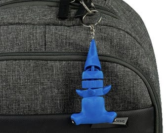 Könnte beinhalten: Ein blauer Plastik-Haifisch-Schlüsselanhänger, der an einem silbernen Schlüsselring hängt, der an einem grauen Rucksack befestigt ist.