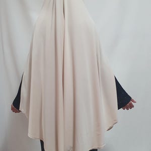 Könnte beinhalten: Ein beiger Hijab mit einem langen, fließenden Design. Der Hijab ist über Kopf und Schultern gelegt, und der Stoff ist glatt und seidig.