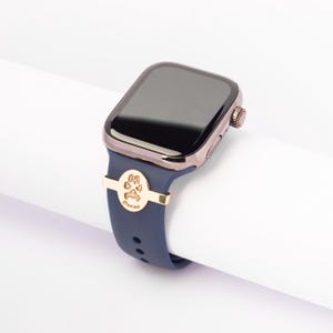 May include: A navy blue Apple Watch band with a gold paw print charm and the name "Oscar" engraved on it.