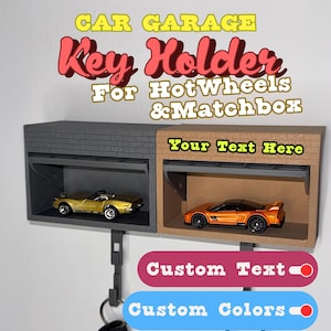 May include: A key holder designed as a car garage, with two bays holding toy cars. The key holder is gray and brown, with the text "CAR GARAGE Key Holder For HotWheels & Matchbox" and "Your Text Here". Includes key rings and the options for custom text and colors.