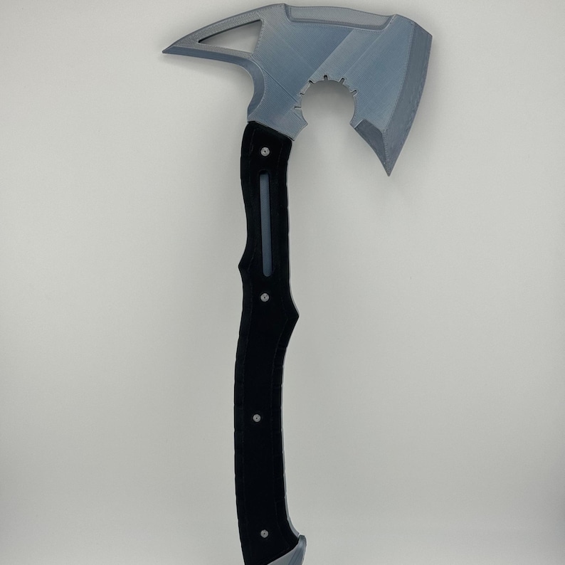 May include: A gray and black axe with a unique design. The axe head is gray with a curved blade and a pointed end. The handle is black with a textured grip and silver rivets. The axe has a modern, industrial aesthetic.