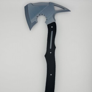 May include: A gray and black axe with a unique design. The axe head is gray with a triangular opening and a sharp blade. The handle is black with a textured grip and a straight gray line down the center. The axe is a tool or decorative item.