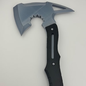 May include: A gray and black axe with a textured blade and a black handle. The axe head has a unique cutout design and a pointed edge. The handle is secured with two rivets.