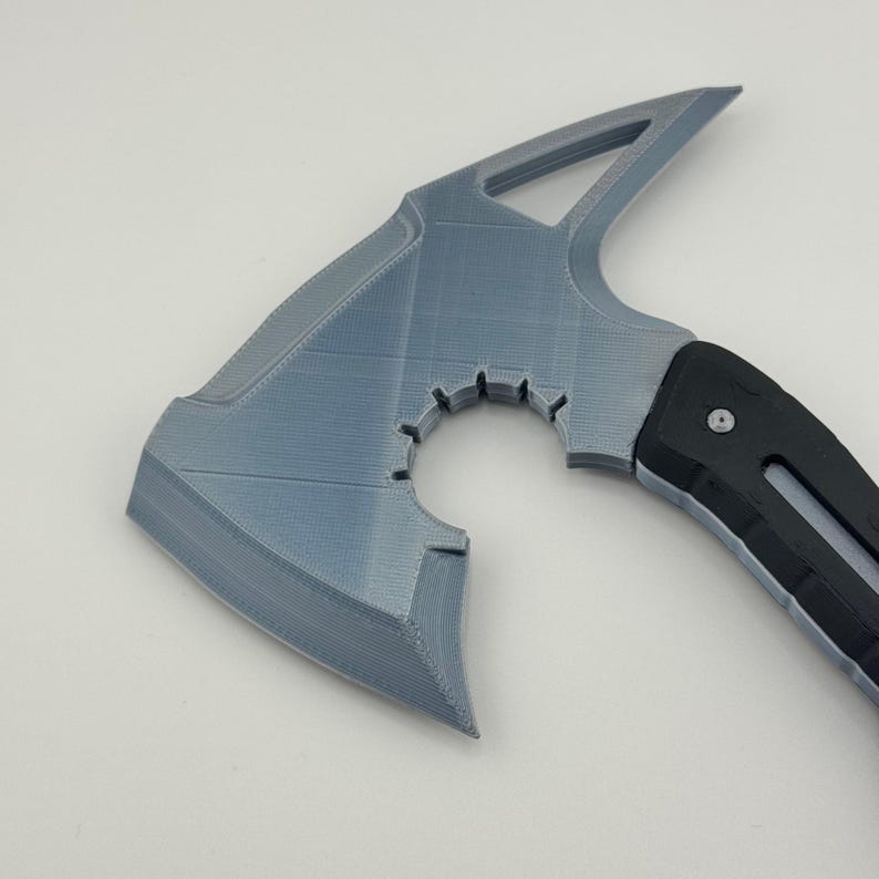 May include: A gray and black axe with a unique design. The axe head is gray with a distinctive shape, featuring a circular cutout and a pointed top. The handle is black and ergonomically designed.