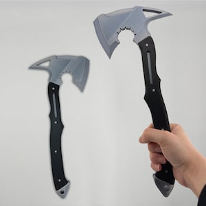 Pode incluir: Dois machados cinza e pretos. As cabeças dos machados têm um design único com uma lâmina curva e uma ponta afiada. Os cabos são pretos com uma pega texturizada. Um machado é segurado por uma mão. Os machados são exibidos em um fundo branco liso.
