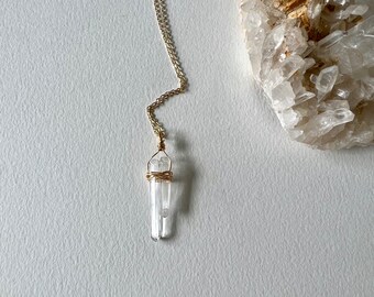 May include: A gold chain necklace with a clear quartz crystal pendant wrapped in gold wire.