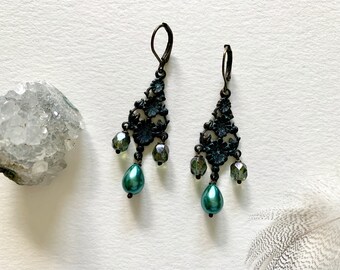 May include: A pair of dangle earrings with a black filigree design and green glass beads. The earrings have a teardrop-shaped pearl at the bottom.