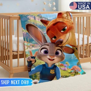 May include: A colorful blanket featuring Judy Hopps and Nick Wilde from Zootopia. The blanket is draped over a wooden crib. The text "MADE IN USA" is visible in the upper right corner. The text "SHIP NEXT DAY" is visible at the bottom.