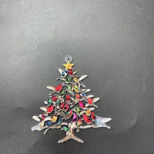 May include: A Christmas tree ornament in the shape of a tree, adorned with colorful birds. The tree is made of metal and has a star at the top. The birds are various colors, including red, green, and blue.