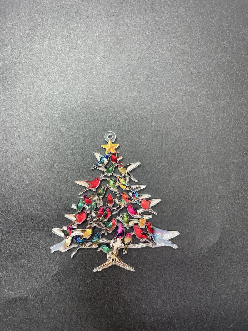 May include: A Christmas tree ornament in the shape of a tree, adorned with colorful birds. The tree is made of metal and has a star at the top. The birds are various colors, including red, green, and blue.