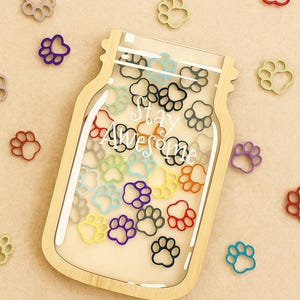 May include: A wooden jar-shaped shadow box with a clear front, filled with colourful paw print cutouts. The text "Stay Awesome" is visible inside. Scattered paw prints in various colours surround the jar.