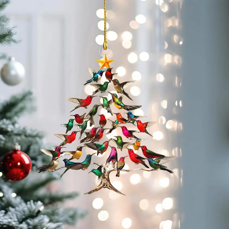 May include: A Christmas tree ornament shaped like a tree, adorned with colorful hummingbird figurines. The ornament is suspended by a gold string and features a gold star at the top. The hummingbirds are in various colors, including red, green, and blue.