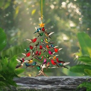 May include: A decorative Christmas tree ornament shaped like a tree, adorned with colorful hummingbirds. The birds are in various poses, with wings spread. A gold star tops the tree, suspended by a gold string.