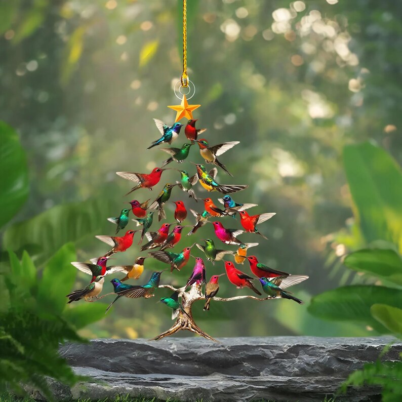 May include: A decorative Christmas tree ornament shaped like a tree, adorned with colorful hummingbirds. The birds are in various poses, with wings spread. A gold star tops the tree, suspended by a gold string.