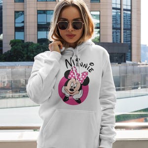 May include: White hooded sweatshirt featuring a Minnie Mouse graphic. The graphic includes Minnie's face, a pink bow, and the name "Minnie" in a playful font. The sweatshirt has a front pocket and a drawstring hood.