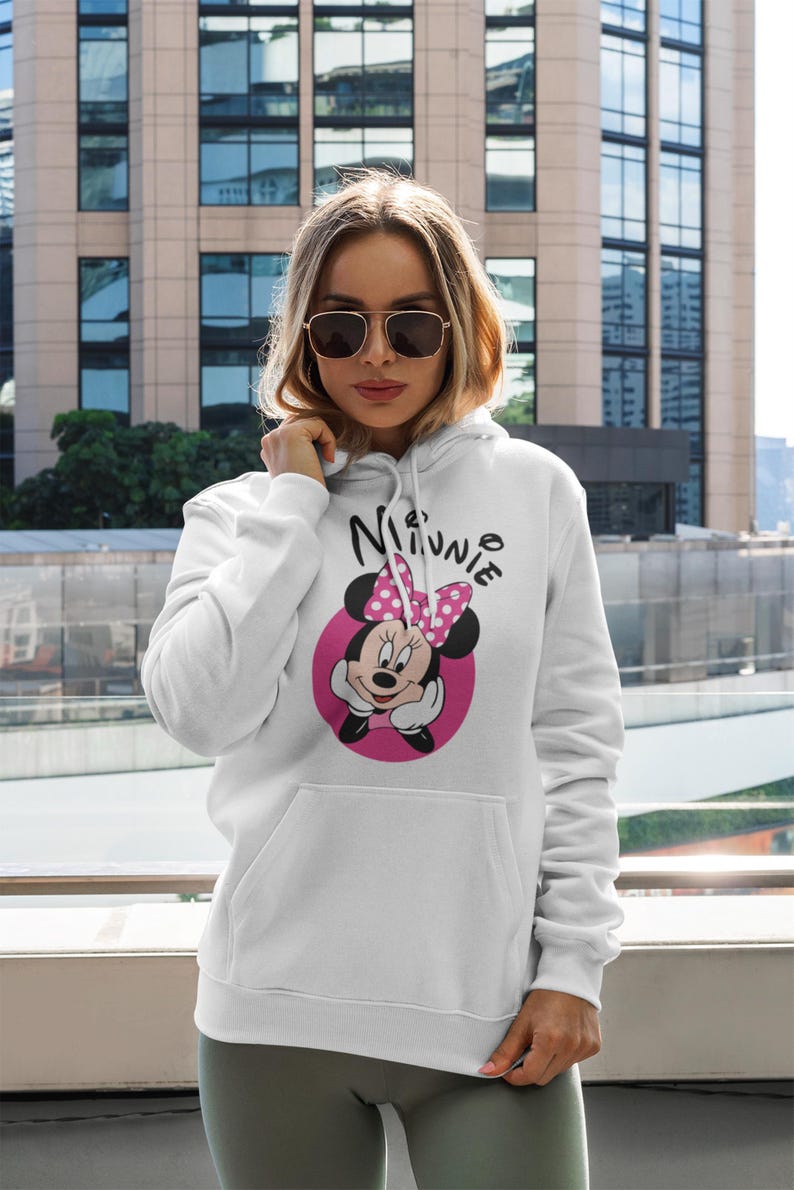 May include: White hooded sweatshirt featuring a Minnie Mouse graphic. The graphic includes Minnie's face, a pink bow, and the name "Minnie" in a playful font. The sweatshirt has a front pocket and a drawstring hood.