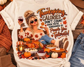 May include: A cream-colored t-shirt featuring a graphic of a person with blonde hair, sunglasses, and a leopard print headband holding a wine glass. The text reads: Thanksgiving Calories Don't Count When You're Surrounded By People You Tolerate.