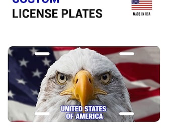 May include: Custom license plate featuring a close-up of a bald eagle with a yellow beak and intense gaze. The background includes the American flag. The text "UNITED STATES OF AMERICA" is displayed below the eagle.