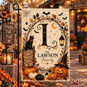 May include: A rectangular garden flag featuring a large letter L, a black cat, a witch hat, pumpkins, and autumn leaves. The text reads The Lawson Family, Grateful, Thankful, Blessed, Together. The design includes a spider web, bats, and a lantern.
