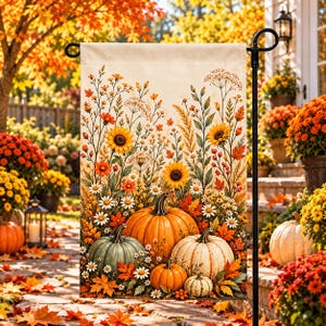 May include: A rectangular garden flag featuring a seasonal autumn illustration of four pumpkins in shades of orange, green, and cream, surrounded by sunflowers, white daisies, orange wildflowers, and fall foliage on a light cream background.