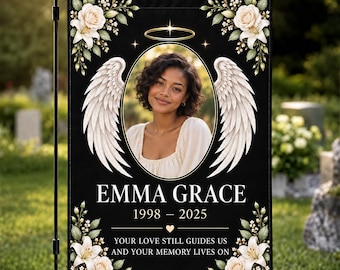 May include: A black memorial garden flag featuring a central oval portrait of a person with white angel wings and a gold halo. The text reads EMMA GRACE 1998-2025 and YOUR LOVE STILL GUIDES US AND YOUR MEMORY LIVES ON, framed by white floral accents.
