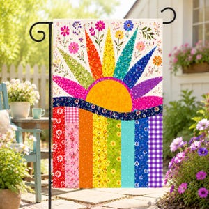 May include: A rectangular garden flag featuring a vibrant sun design with radiating colorful rays in red, orange, yellow, green, blue, and purple. The lower section displays vertical stripes of various floral and gingham patterns in a rainbow palette.